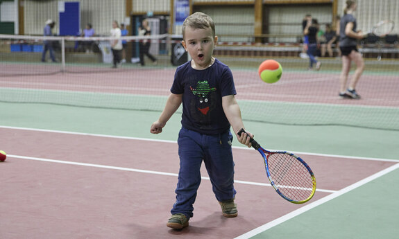 Ein kleiner Junge spielt in der Halle Tennis