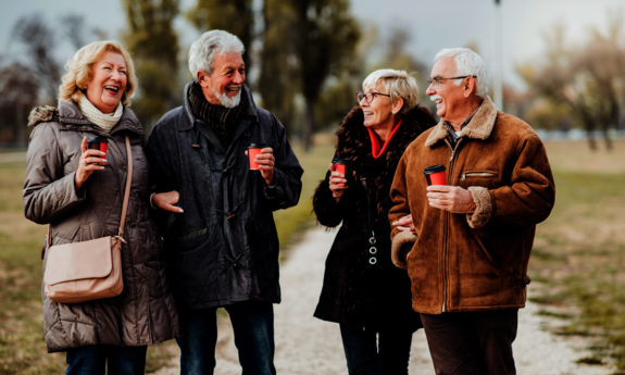 Vier ältere Menschen spazieren auf einem Feldweg im Winter und unterhalten sich lachend.